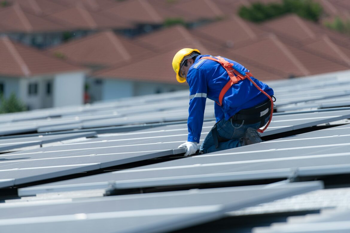 A technician is installing solar panels on the roof of the warehouse