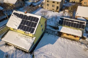 House roof covered with solar panels in winter with snow on top. Energy efficiency and maintenance